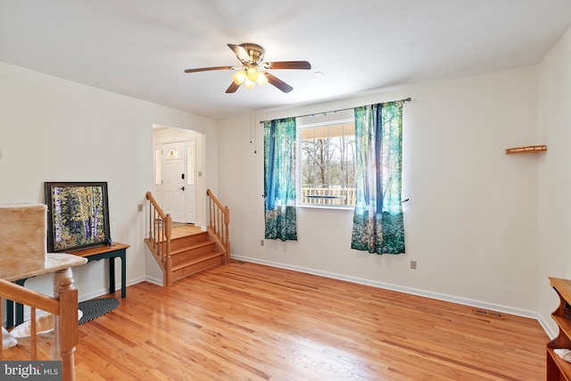 living area with light wood-type flooring, visible vents, stairway, baseboards, and ceiling fan