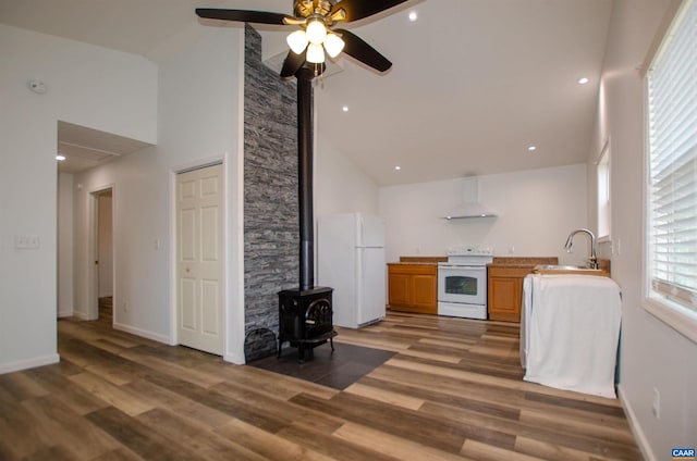 kitchen featuring a sink, wood finished floors, range hood, white appliances, and a wood stove