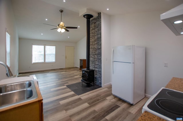 kitchen featuring white appliances, baseboards, a wood stove, a sink, and light wood-style floors