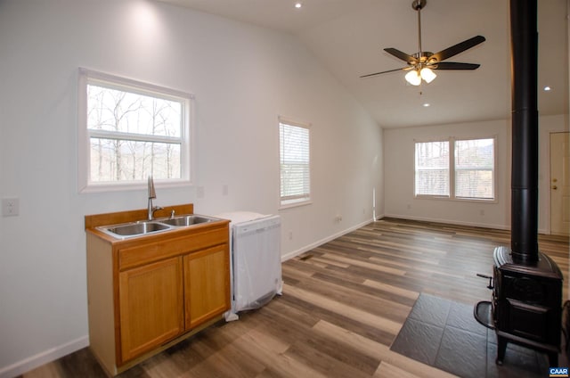 kitchen with dishwasher, light wood-type flooring, vaulted ceiling, a wood stove, and a sink