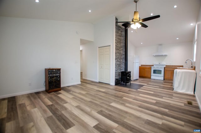 unfurnished living room featuring high vaulted ceiling, a sink, light wood finished floors, baseboards, and a wood stove