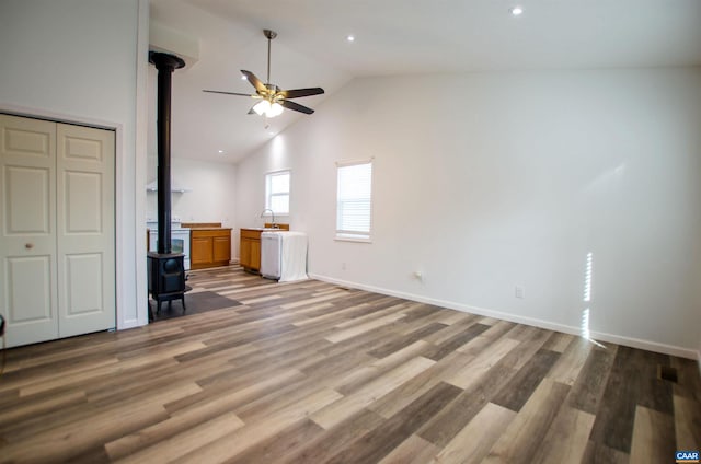 unfurnished living room featuring lofted ceiling, a ceiling fan, wood finished floors, baseboards, and a wood stove