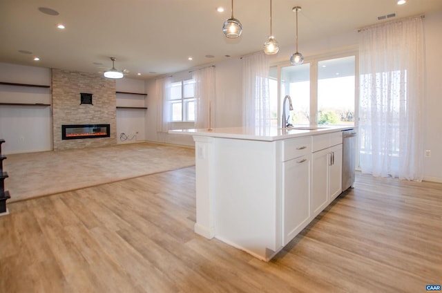 kitchen featuring visible vents, light wood-style flooring, a sink, a stone fireplace, and white cabinetry