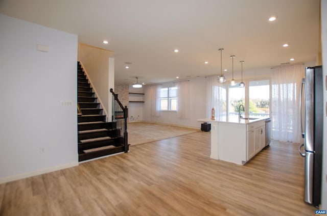 kitchen featuring light wood-style flooring, a sink, open floor plan, stainless steel appliances, and white cabinets