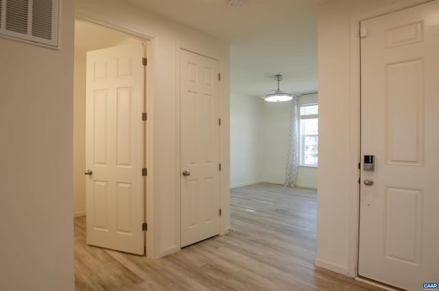 hallway featuring baseboards, visible vents, and light wood finished floors