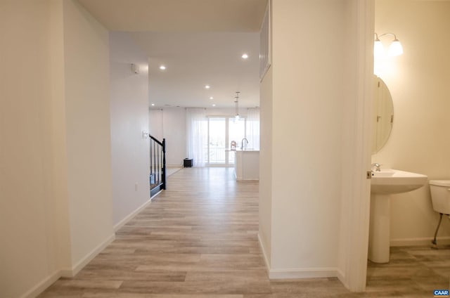 hallway with recessed lighting, light wood-type flooring, baseboards, and a sink