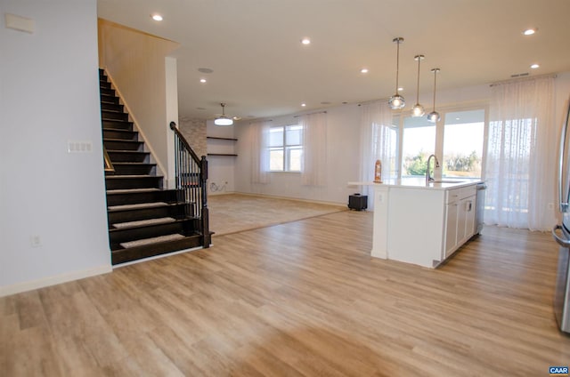 kitchen with a center island with sink, light wood finished floors, recessed lighting, a sink, and white cabinetry