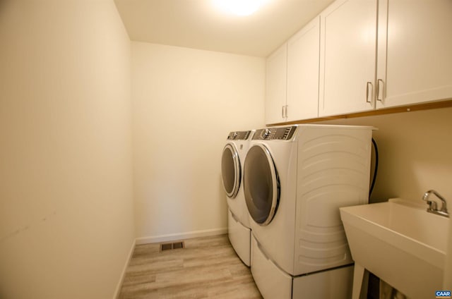 washroom featuring visible vents, washer and clothes dryer, a sink, cabinet space, and baseboards