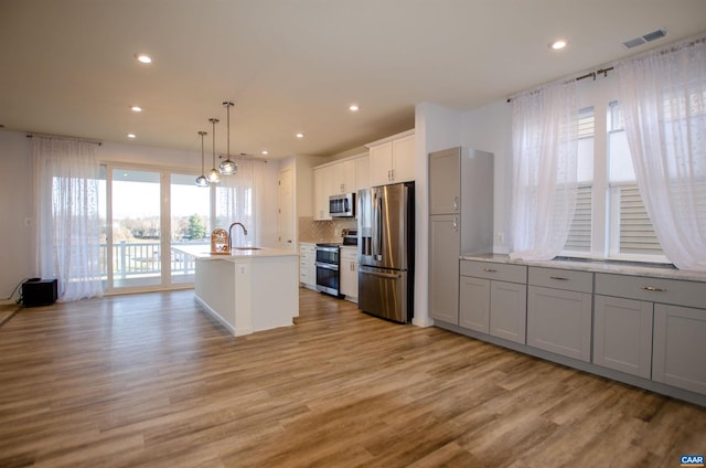 kitchen with backsplash, visible vents, light wood-style floors, and appliances with stainless steel finishes