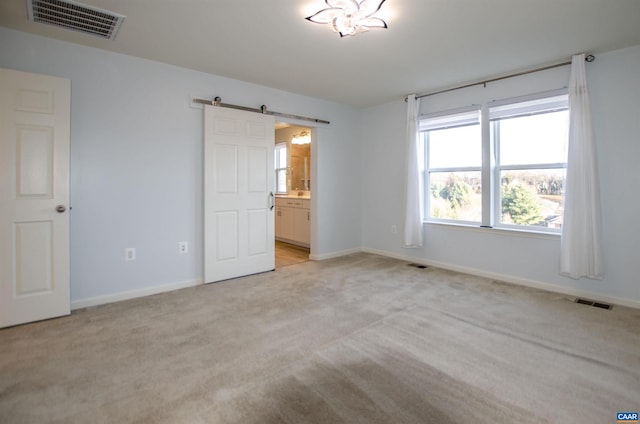 unfurnished bedroom with baseboards, visible vents, a barn door, and light carpet