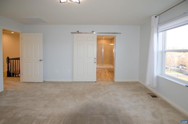 unfurnished bedroom featuring visible vents, a barn door, and carpet floors