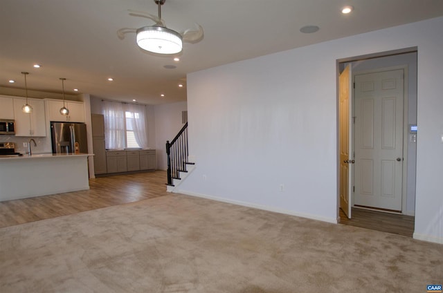 unfurnished living room featuring a sink, recessed lighting, baseboards, light colored carpet, and stairs