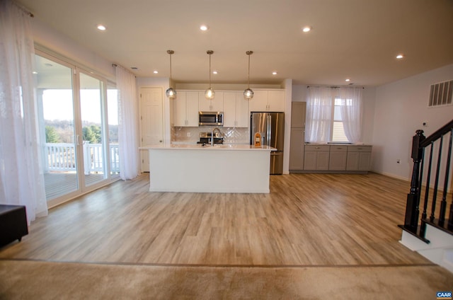 kitchen with visible vents, a kitchen island with sink, light wood-style flooring, stainless steel appliances, and decorative backsplash