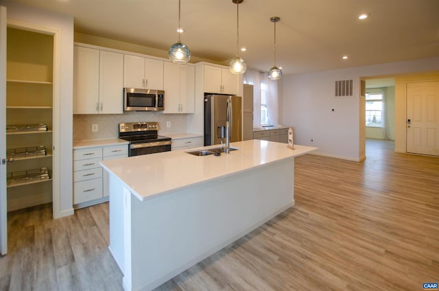 kitchen with visible vents, an island with sink, a sink, stainless steel appliances, and white cabinets