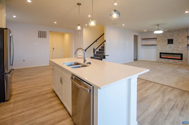 kitchen featuring visible vents, a sink, stainless steel appliances, light wood-style floors, and a large fireplace