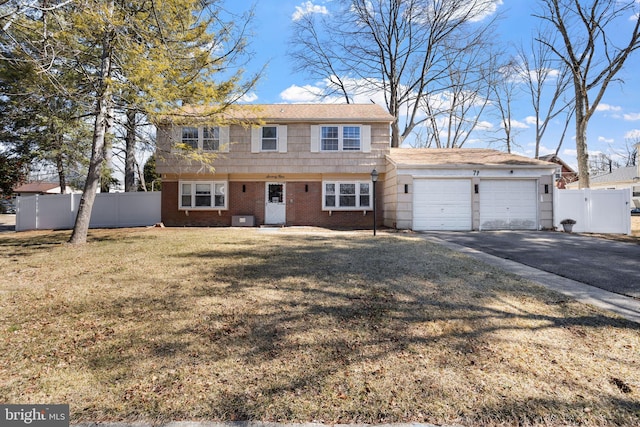 colonial inspired home featuring brick siding, aphalt driveway, a garage, and fence