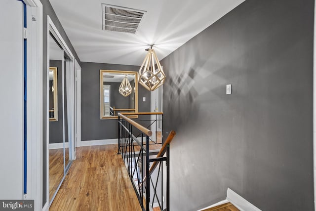 interior space featuring visible vents, an upstairs landing, wood finished floors, an inviting chandelier, and baseboards