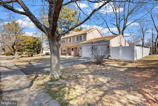 colonial home featuring a gate, fence, driveway, a garage, and brick siding