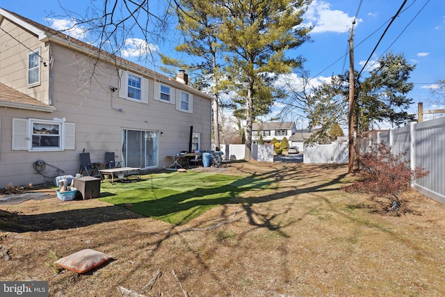 back of property with fence, a lawn, and a chimney