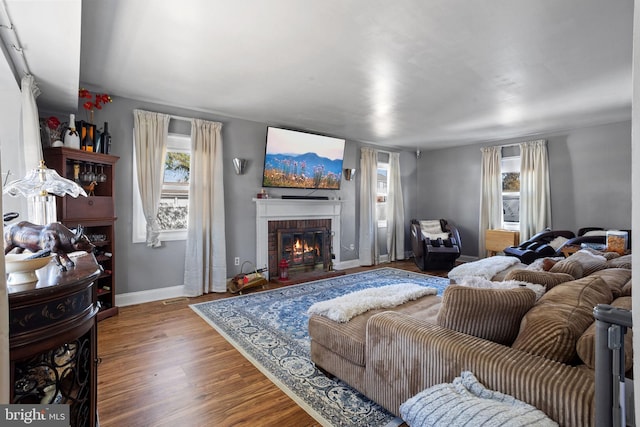 living room featuring visible vents, a brick fireplace, baseboards, and wood finished floors