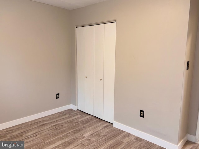 unfurnished bedroom featuring a closet, baseboards, and light wood finished floors