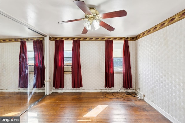 empty room featuring baseboards, hardwood / wood-style flooring, a ceiling fan, and wallpapered walls