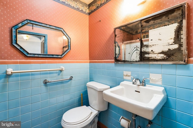 half bath featuring wallpapered walls, a wainscoted wall, and a sink