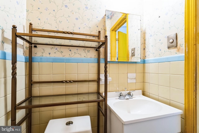 half bath featuring a wainscoted wall, tile walls, vanity, and wallpapered walls