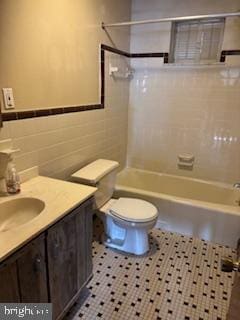 full bath featuring tile patterned flooring, tub / shower combination, toilet, vanity, and tile walls