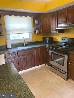 kitchen with under cabinet range hood, a sink, dark stone counters, light tile patterned flooring, and stainless steel electric range oven