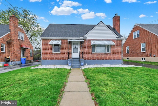 bungalow with a front yard, a shingled roof, and brick siding