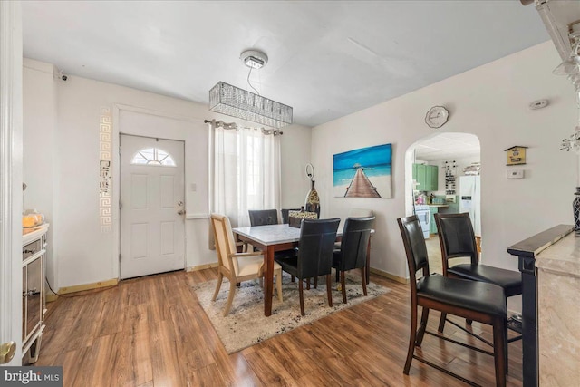 dining space featuring wood finished floors, arched walkways, and baseboards