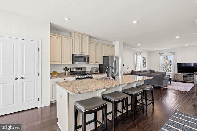 kitchen with a breakfast bar, a sink, dark wood-type flooring, appliances with stainless steel finishes, and cream cabinets