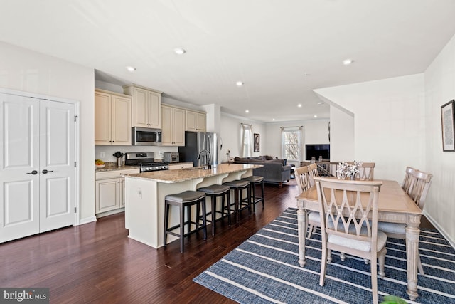 kitchen featuring a kitchen bar, cream cabinetry, a kitchen island with sink, open floor plan, and appliances with stainless steel finishes