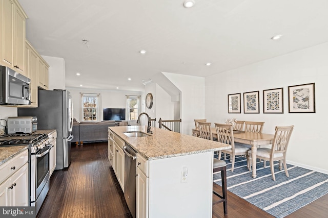 kitchen featuring open floor plan, a breakfast bar, appliances with stainless steel finishes, cream cabinetry, and a sink