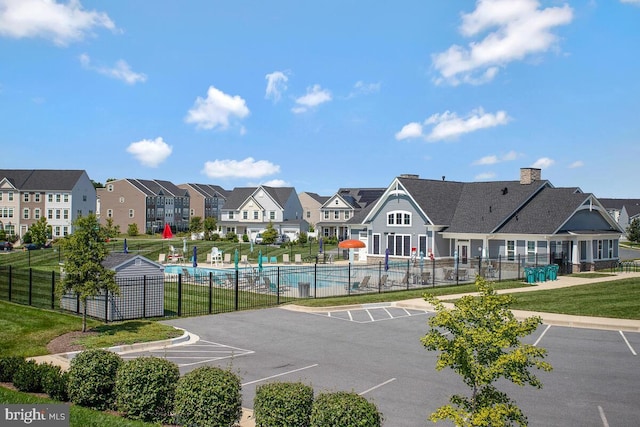 view of home's community featuring a pool, fence, a residential view, a lawn, and uncovered parking