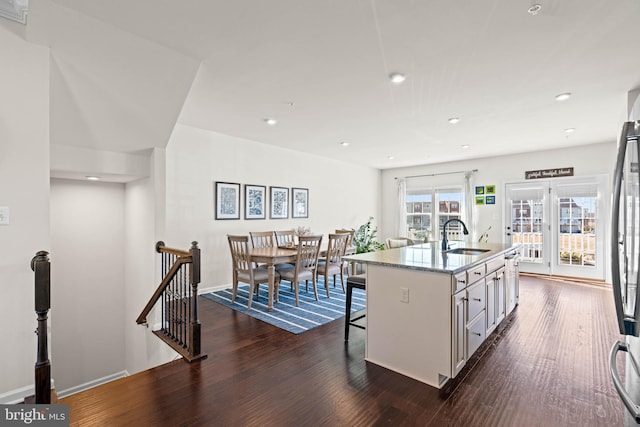 kitchen with a breakfast bar area, light stone counters, dark wood-style flooring, and a sink