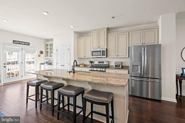 kitchen featuring a sink, a kitchen bar, cream cabinetry, stainless steel appliances, and dark wood-style flooring