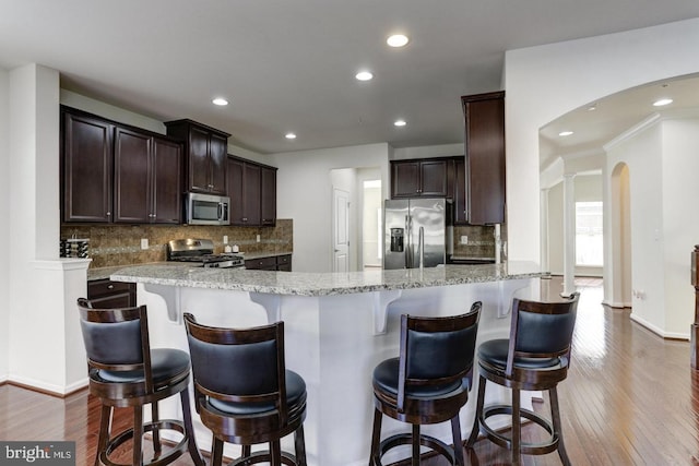 kitchen featuring light stone counters, appliances with stainless steel finishes, dark wood-style flooring, and dark brown cabinets