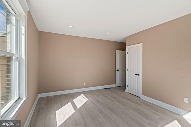 spare room featuring a wealth of natural light, baseboards, and light wood-style floors