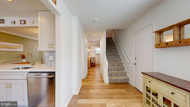 kitchen with light wood-type flooring, a sink, stainless steel dishwasher, backsplash, and white cabinets