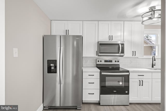 kitchen with a sink, tasteful backsplash, appliances with stainless steel finishes, white cabinets, and light countertops