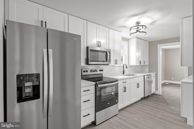 kitchen with a sink, tasteful backsplash, white cabinetry, stainless steel appliances, and light countertops