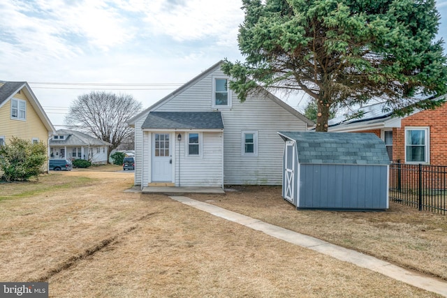 rear view of house featuring fence, a shingled roof, an outdoor structure, a storage unit, and a lawn