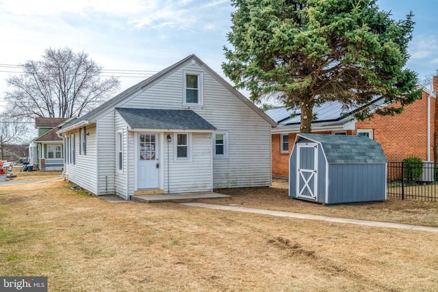 rear view of house featuring fence, roof with shingles, an outdoor structure, a yard, and a storage unit