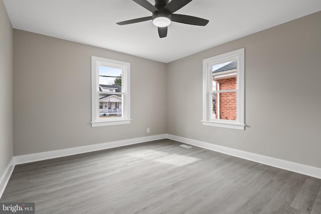 spare room featuring wood finished floors, a healthy amount of sunlight, baseboards, and ceiling fan