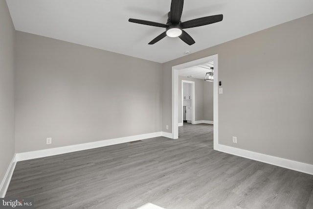 empty room with a ceiling fan, wood finished floors, visible vents, and baseboards