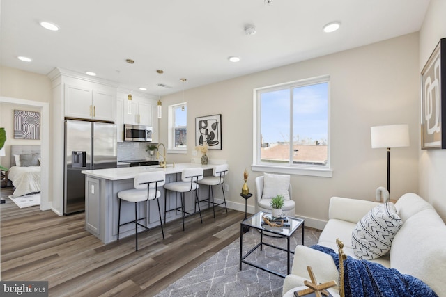 kitchen with wood finished floors, a peninsula, appliances with stainless steel finishes, white cabinetry, and a kitchen breakfast bar