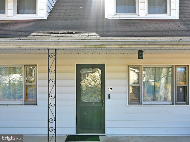 entrance to property featuring covered porch and a shingled roof