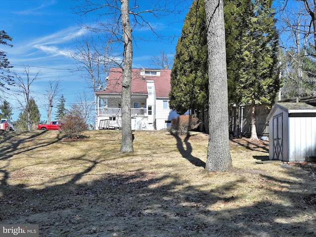 back of property featuring a storage shed, a yard, an outdoor structure, and roof with shingles